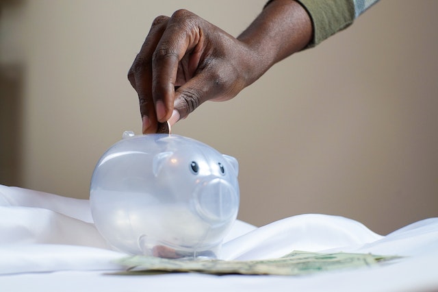 a hand putting money into a clear piggy bank