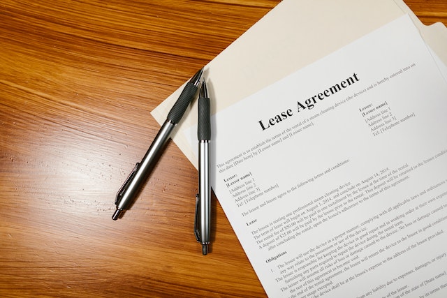 White sheet that reads “Lease Agreement” in black letters, placed on a wooden table next to two black ballpoint pens