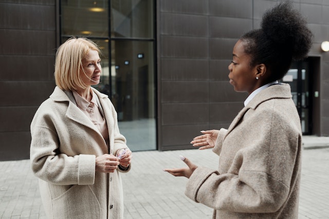 Two people in gray coats talking outside an office building