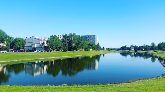 Body of water surrounded by green grass near buildings