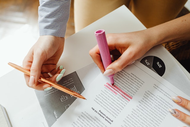 A pair of hands going over some printed documents with a pencil and a pink highlighter