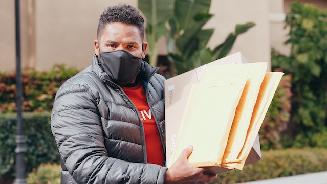 Person wearing a face mask and holding a handful of mail parcels