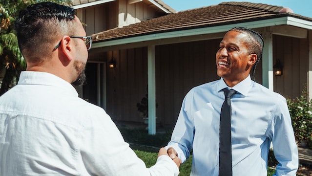 Two people in button-ups shaking hands in front of a residential property