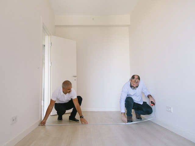 Two people measuring the length of an empty white room