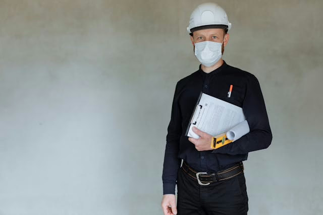 a-contractor-in-a-mask-and-hard-hat-holding-a-clipboard