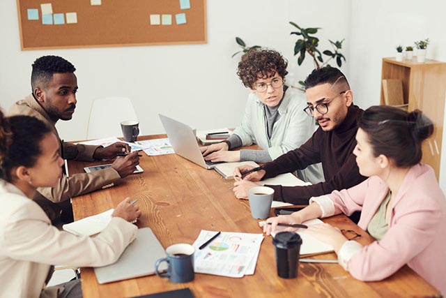 a-team-of-colleagues-discussing-ideas-at-a-wooden-table-with-laptops-charts-and-coffee-cups