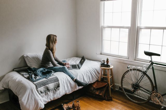 person using their laptop while sitting on a bed
